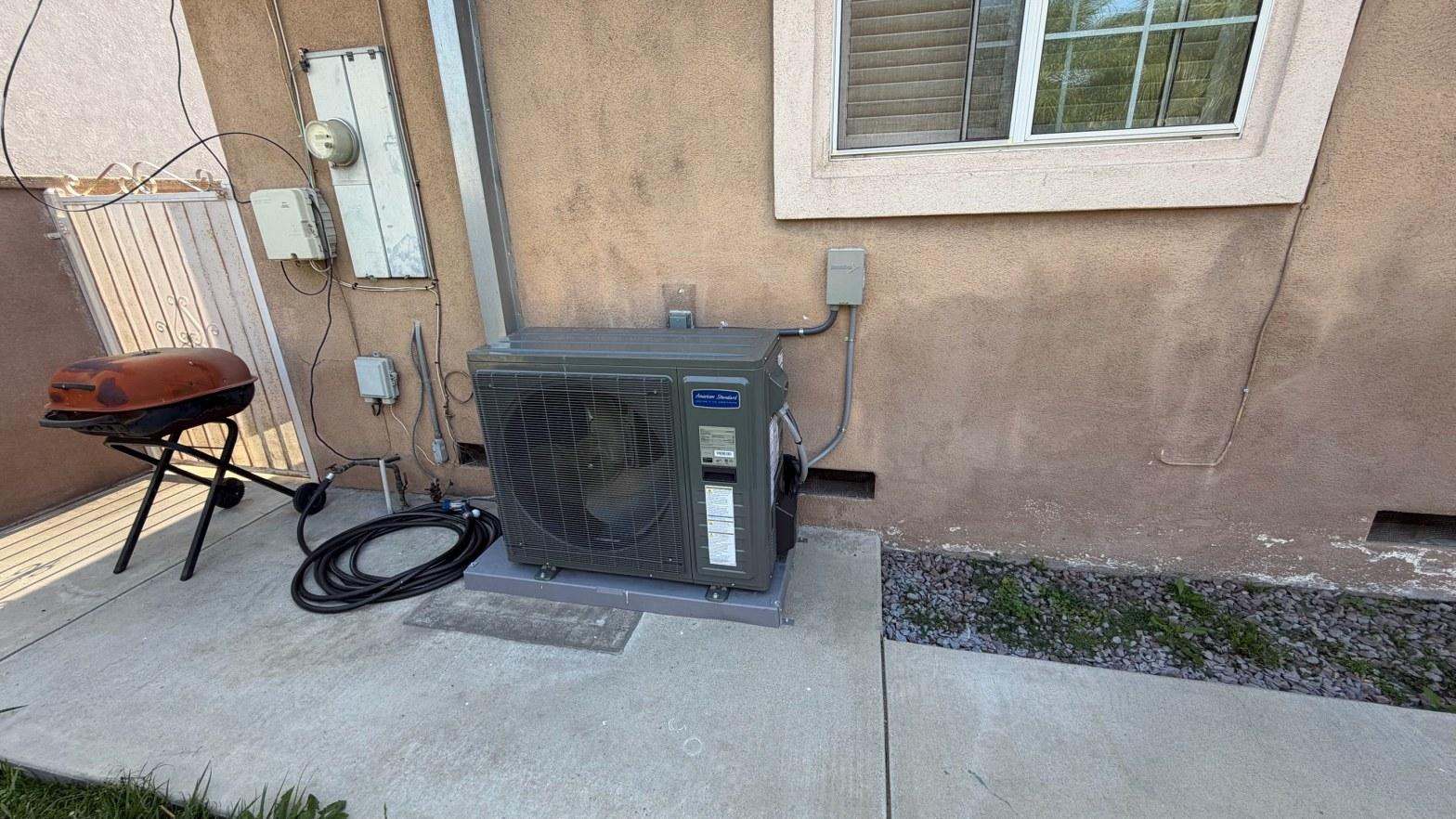 American Standard mini-split heat pump outdoor unit on concrete pad against tan stucco wall with disconnect box.
