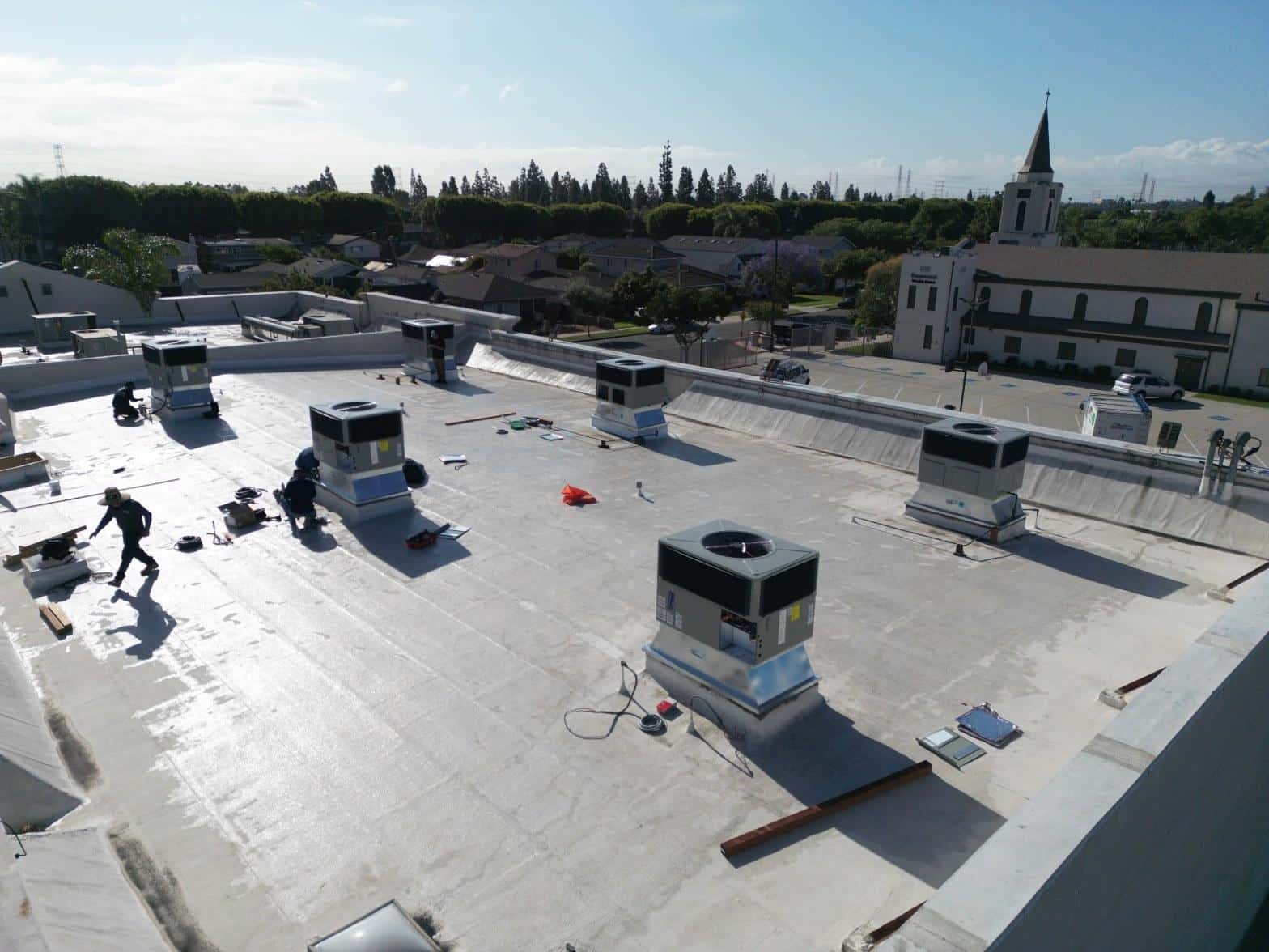 Commercial flat roof with multiple packaged HVAC units being installed by technicians, church steeple visible in background.